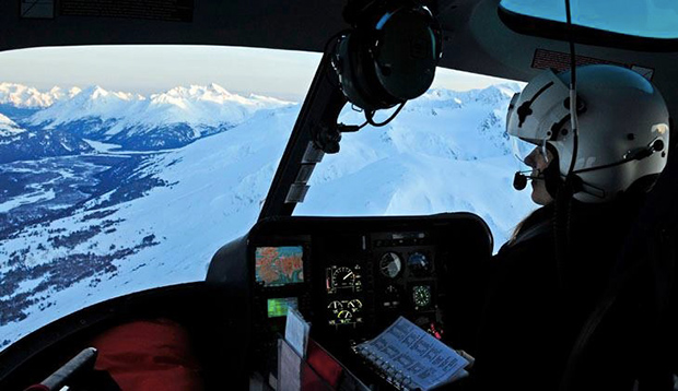 Lorena Knapp in the cockpit of her helicopter with Alaska scenery outside